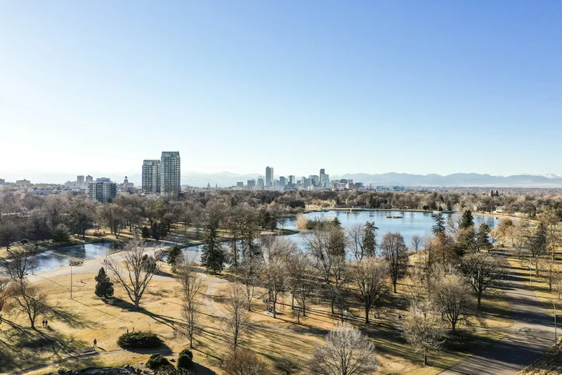 Still park water and mature shade trees on a clear Colorado morning, the same kind of canopy that covers Centennial's older subdivisions