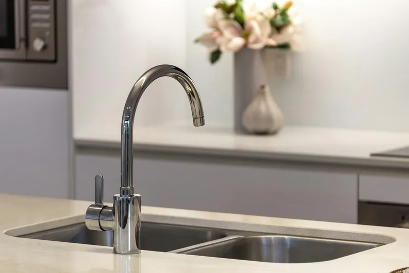 A modern kitchen faucet running clear in a renovated Wheat Ridge brick ranch kitchen