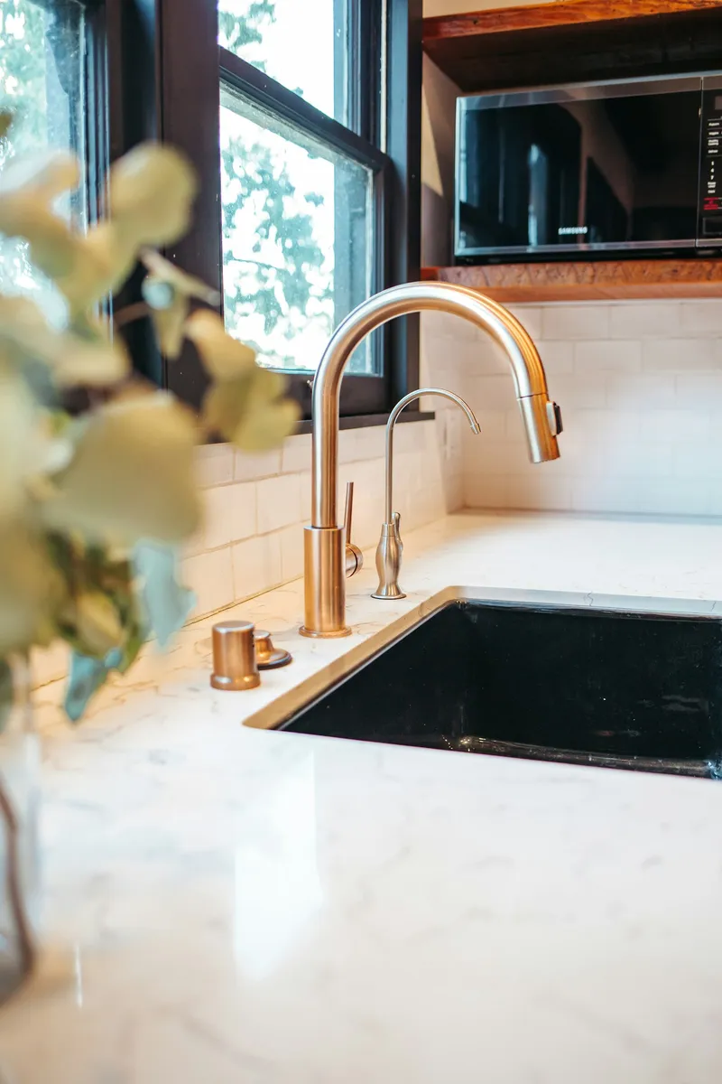 Water running from a kitchen faucet in front of a bright window, the kind of small bungalow kitchen Englewood has by the thousand